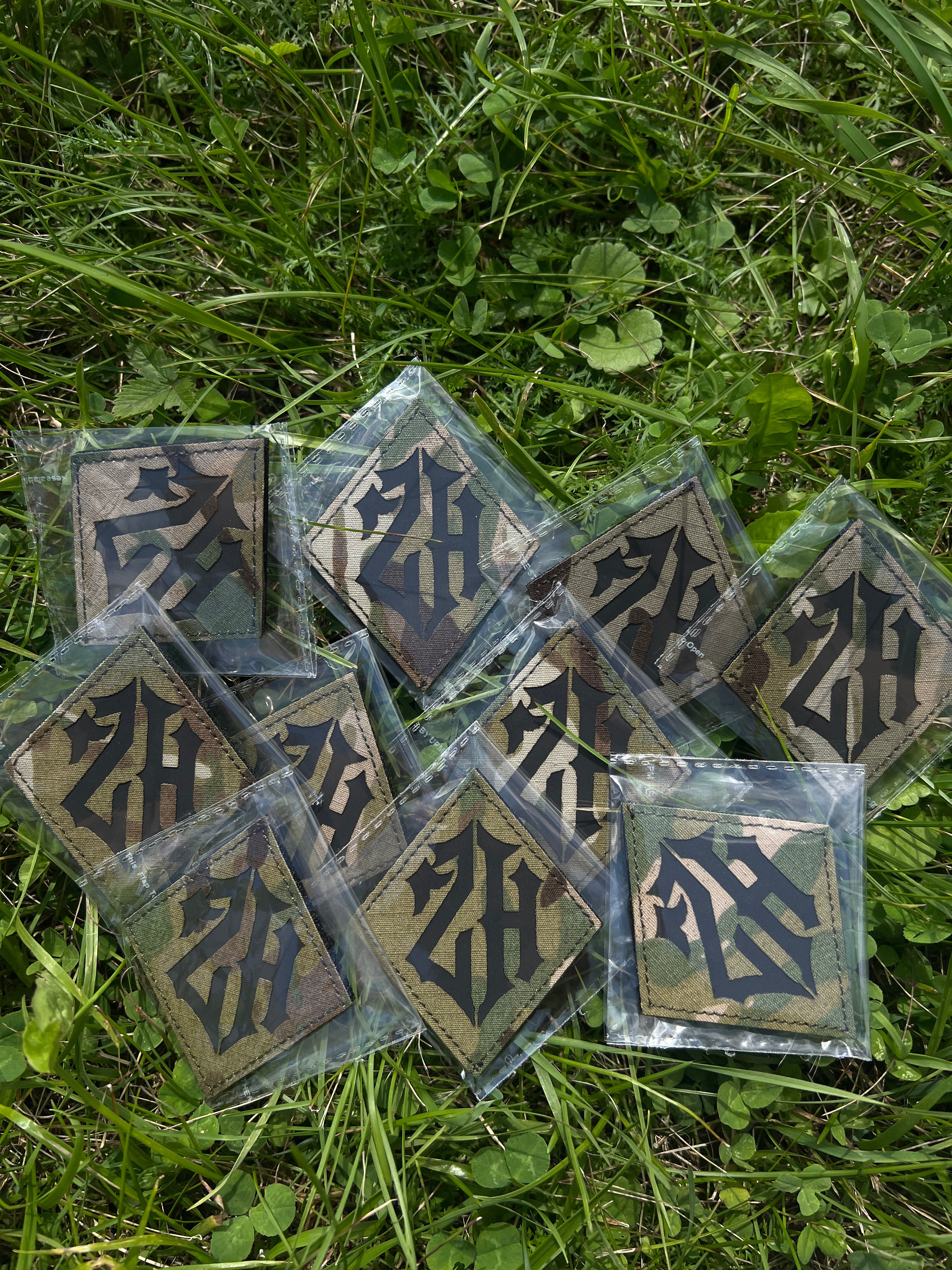 Several square patches with dark gothic lettering Zero Hour logo on a tan background, sealed in clear plastic and scattered on green grass.