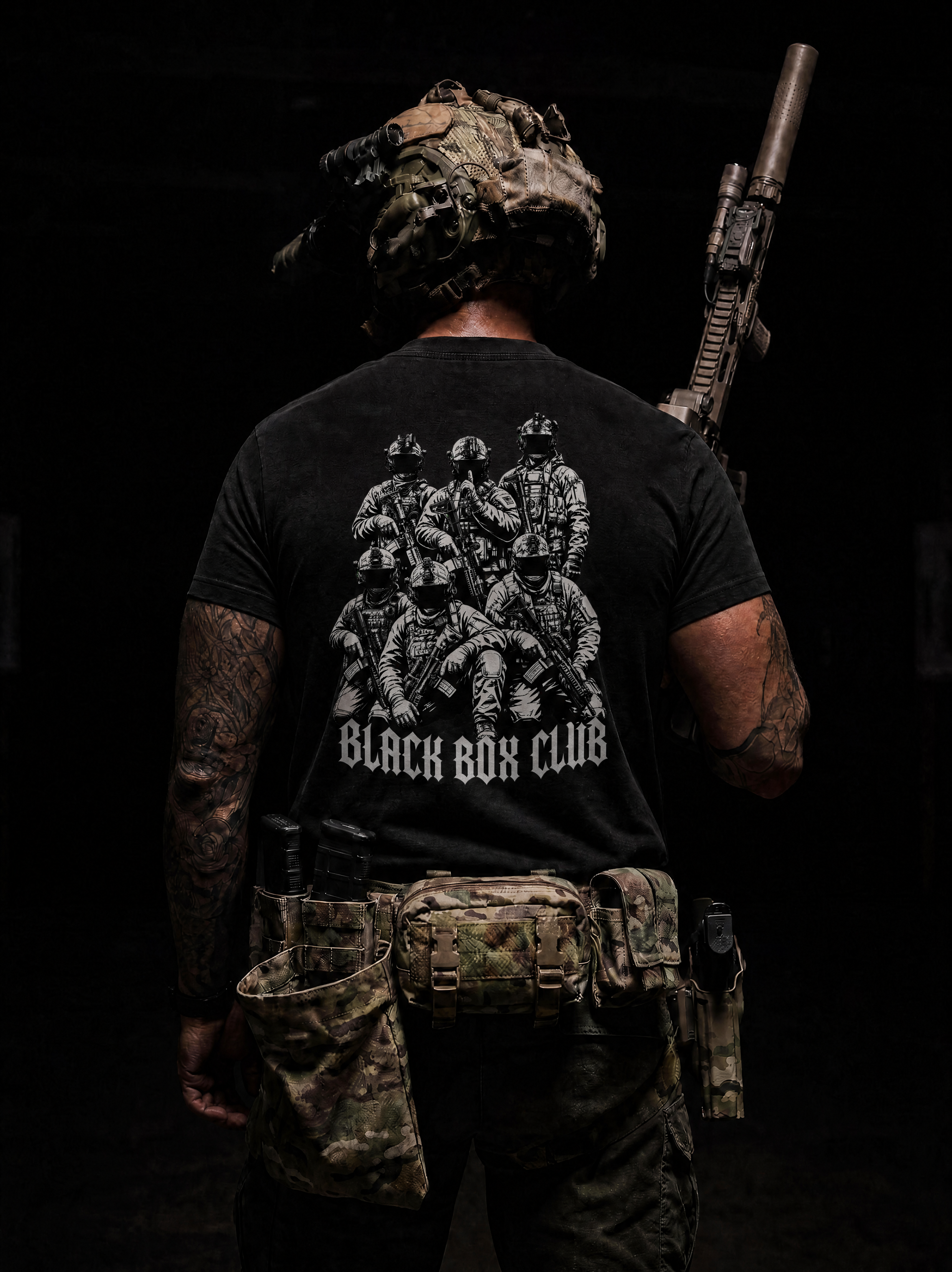 A man viewed from behind wearing a black graphic t-shirt with a white print of soldiers and the text 'BLACK BOX CLUB'. He is also wearing tactical gear, including a camouflage helmet, a rifle over his shoulder, and a tactical belt pouch, set against a very dark background.