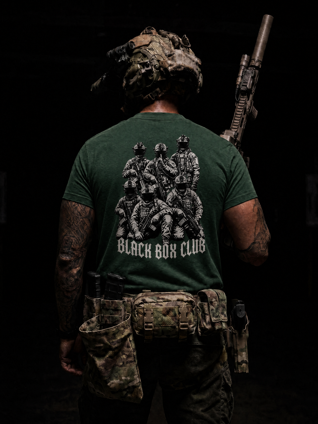 A man viewed from behind wearing a dark green tactical t-shirt with a large black graphic of soldiers and the text 'BLACK BUCK CLUB' on the back, paired with camouflage gear against a dark background.