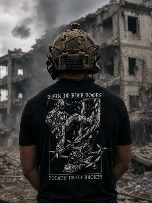 Person wearing a tactical helmet and black t-shirt with a graphic design in front of a destroyed building.