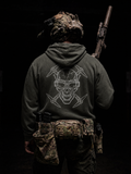 Person wearing a hoodie with a skull design and holding a rifle on a black background