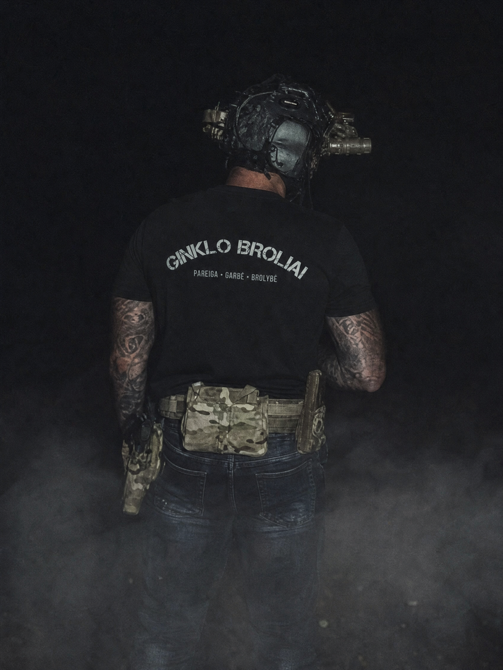 Person wearing a black t-shirt with 'Ginklo Broliai' text, tactical belt, and helmet in a dark setting.