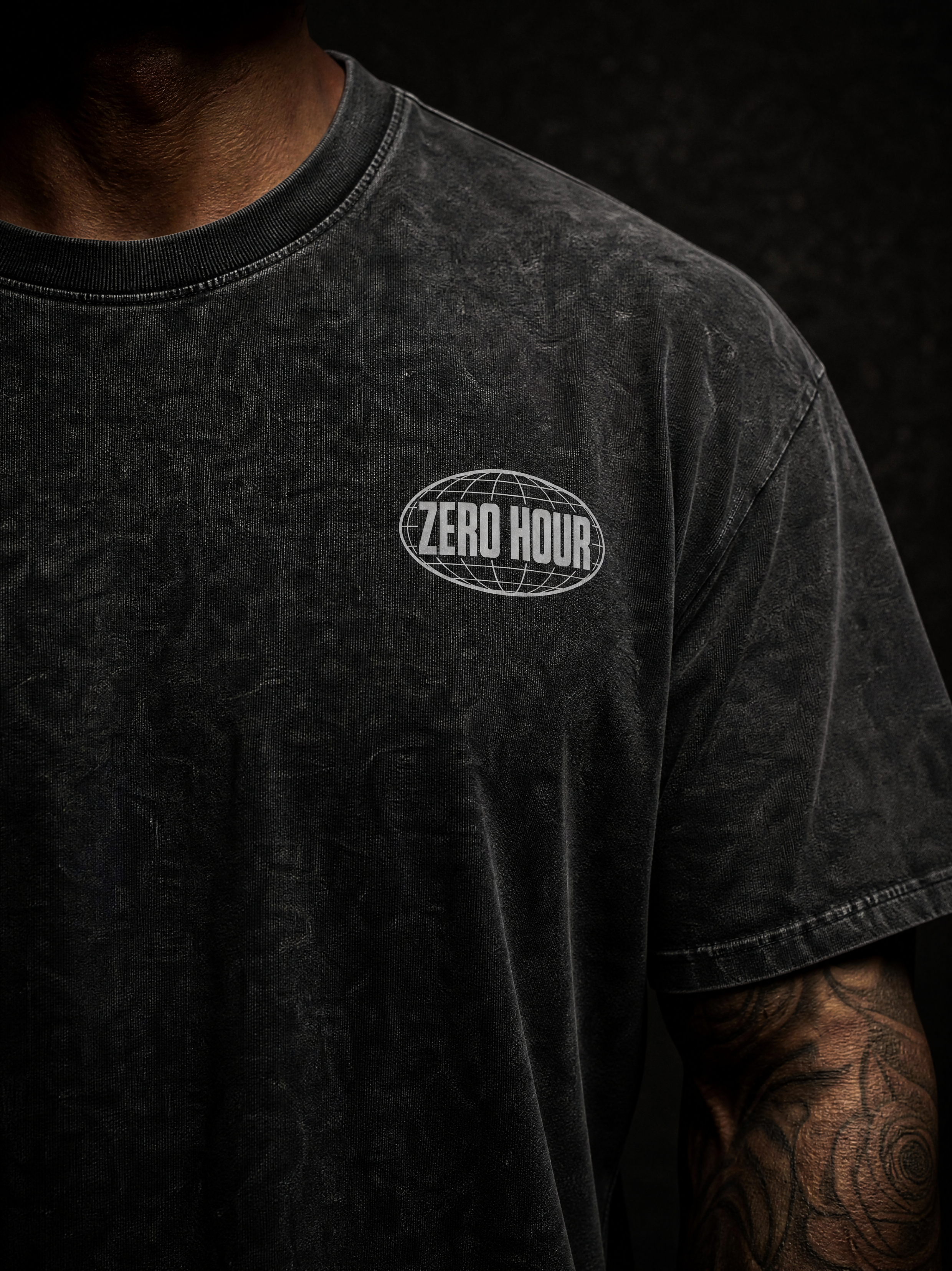 Close-up of a person wearing a dark washed black t-shirt with a white 'ZERO HOUR' oval logo on the chest, set against a dark background.