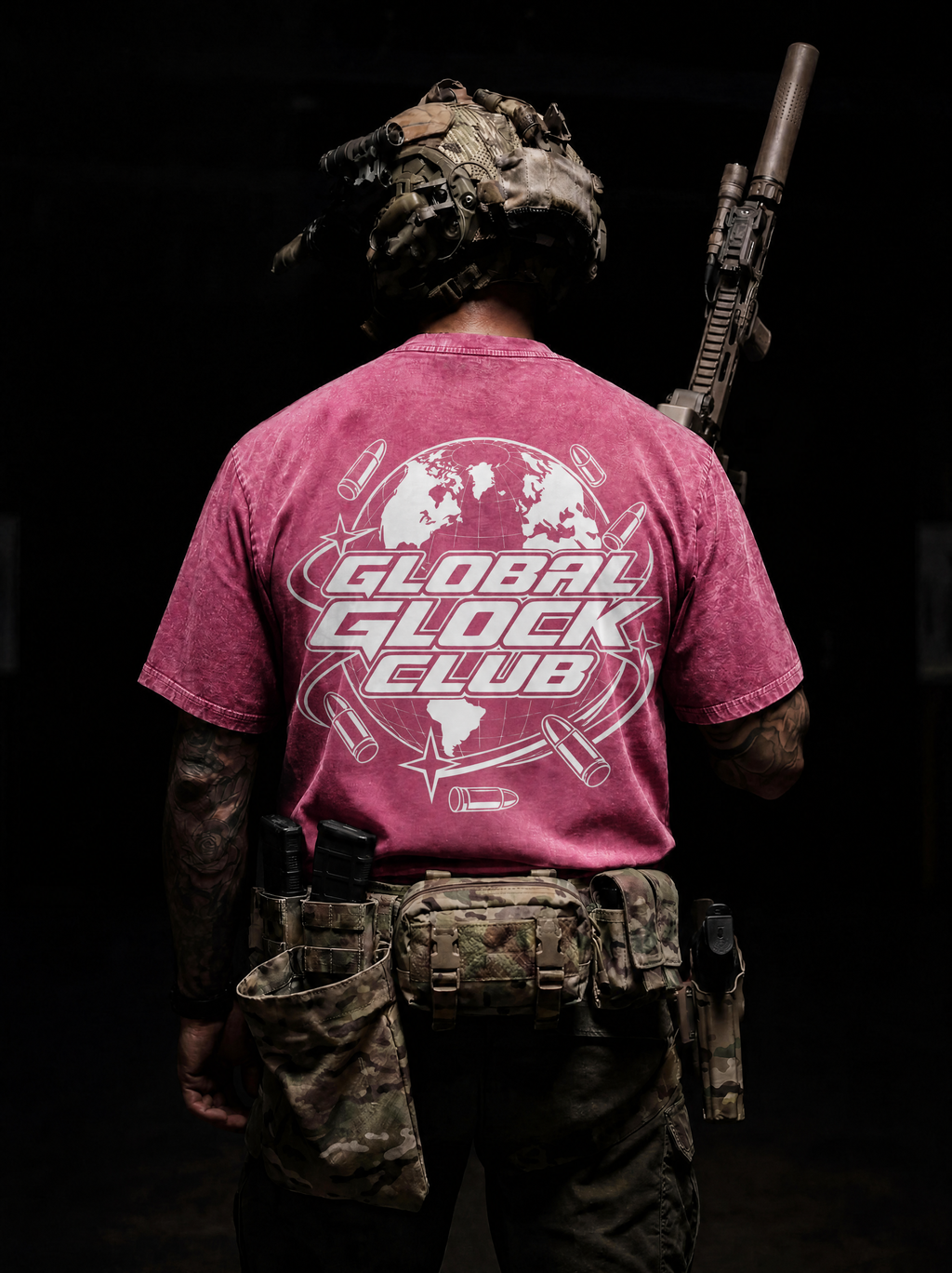A person shown from behind wearing a faded pink t-shirt with a large white 'GLOBAL GLOCK CLUB' graphic on the back, paired with camouflage tactical gear and holding a rifle against a dark background.