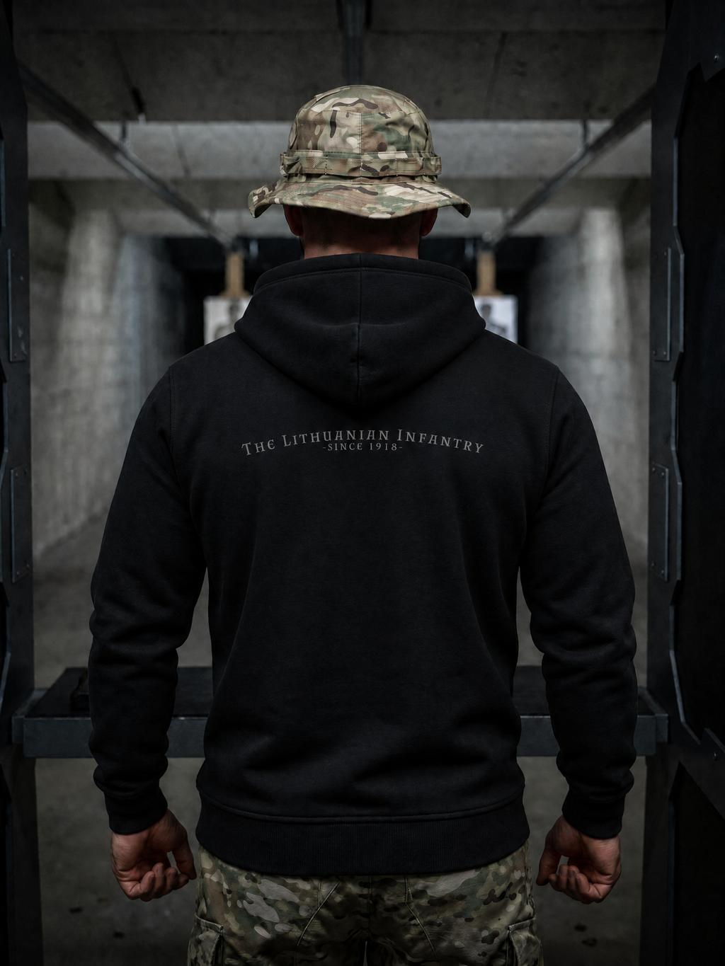 Person wearing a black hoodie with 'The Lithuanian Infantry' text, standing in a dimly lit corridor.