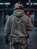 A person viewed from behind wearing a gray hoodie with a large black tactical skull graphic and the words 'Seek and Destroy' on the back, standing in a dim indoor shooting range holding a rifle.
