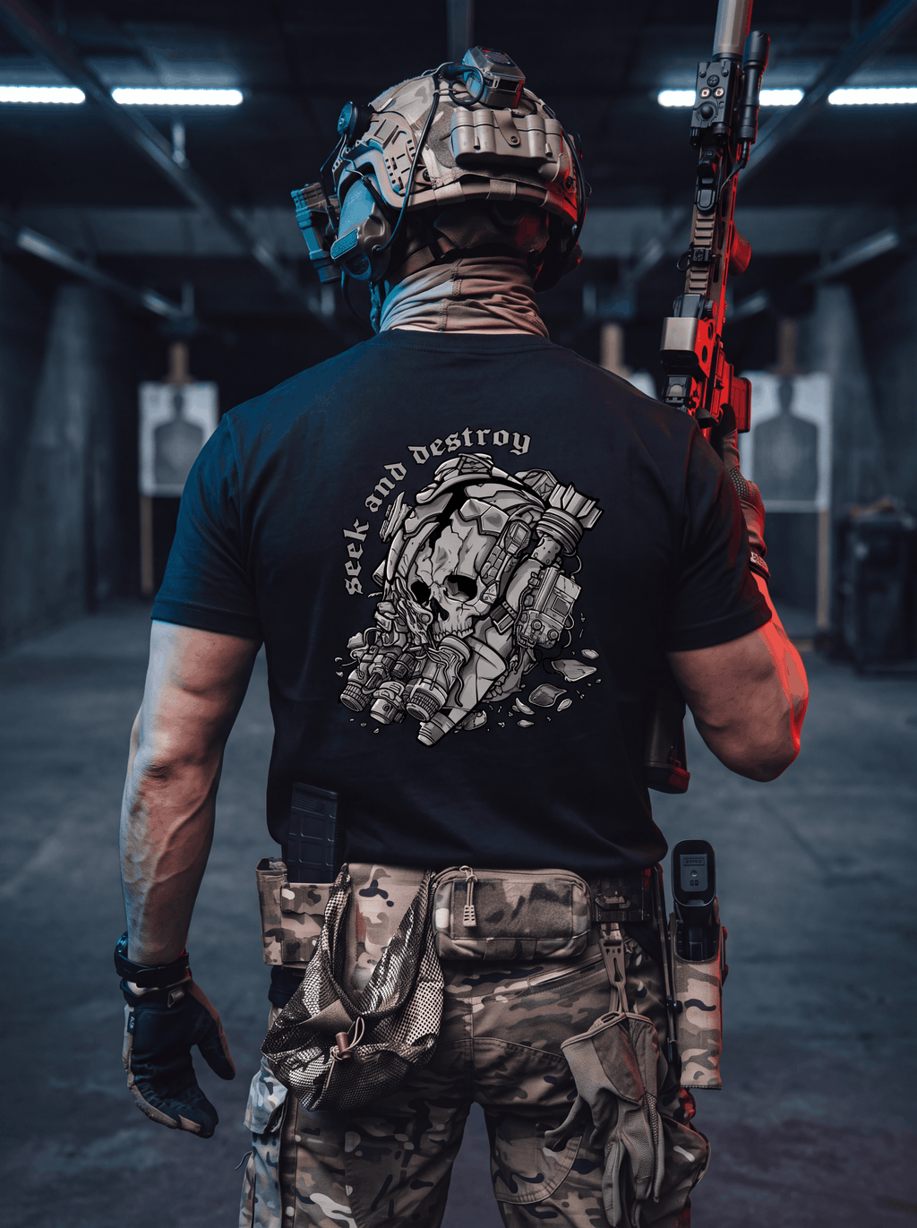 A man viewed from behind wearing a black graphic t-shirt with a white skull design and the words 'seek and destroy' on the back, paired with camouflage tactical pants and a helmet, standing in a shooting range holding a rifle.