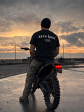 Person standing next to a motorcycle with wind turbines and a sunset in the background